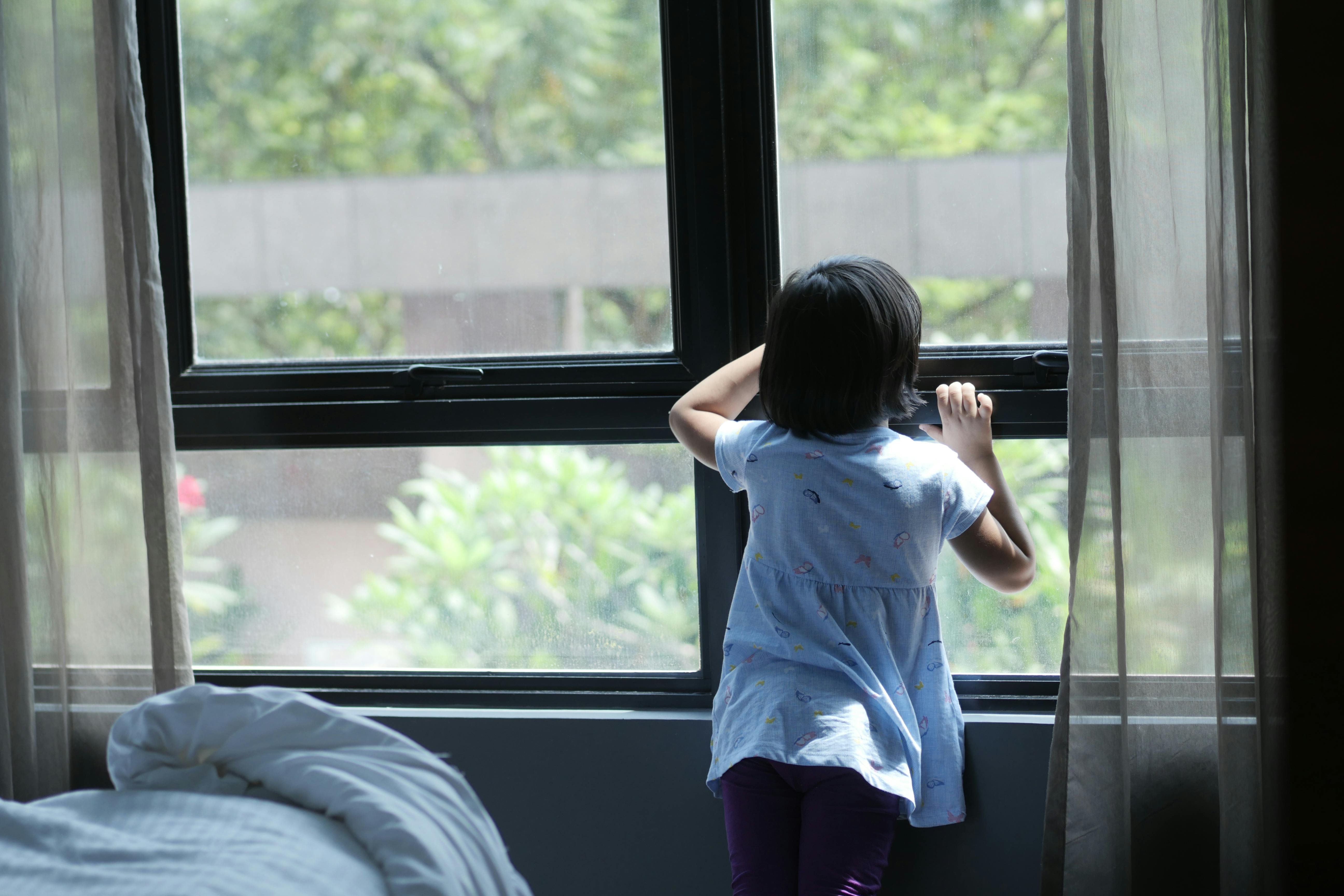Free A young girl gazes thoughtfully out of a window, indoors during the day. Stock Photo