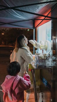 A woman serves ice cream at a street stall under a tent, at night.