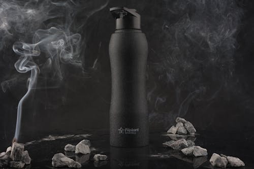 Black Plastic Bottle Among Rocks and Smoke