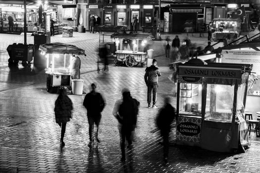 Black and white scene of a bustling night market with blurred silhouettes walking by.