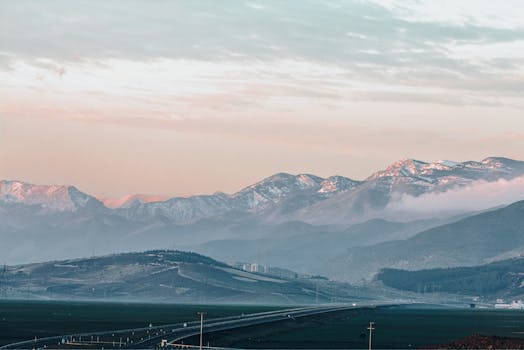 A serene winter landscape of snowcapped mountains and a winding road at dusk.