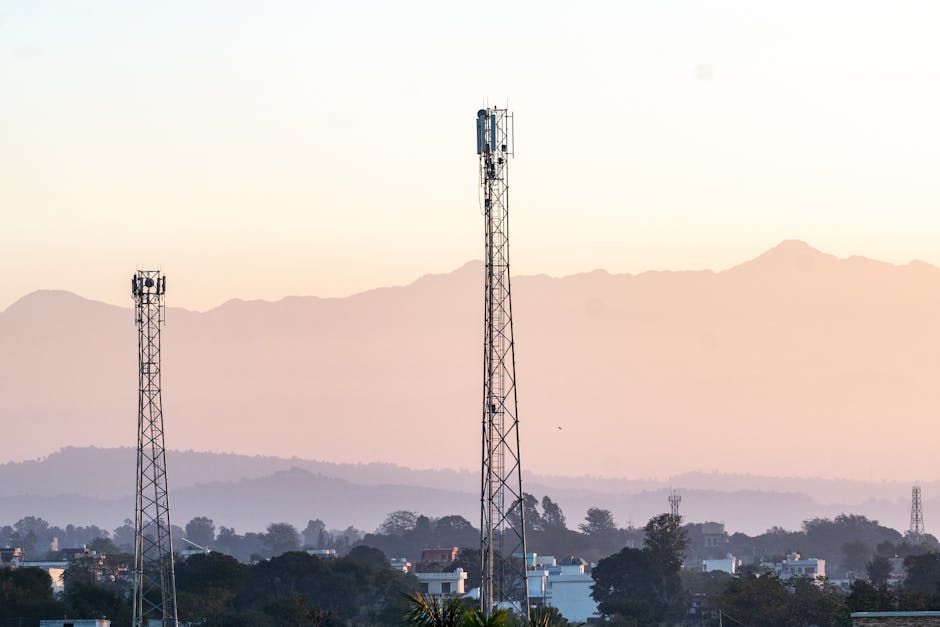 Telecom towers rise above a town against a backdrop of mountains at dawn, highlighting communication infrastructure.