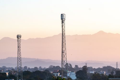 Free Telecom towers rise above a town against a backdrop of mountains at dawn, highlighting communication infrastructure. Stock Photo
