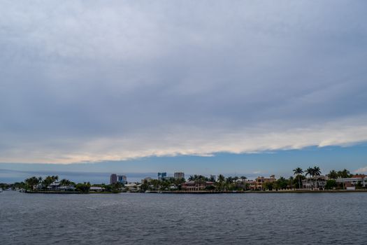 A tranquil coastal scene with tropical waterfront houses and palm trees under a cloudy sky.
