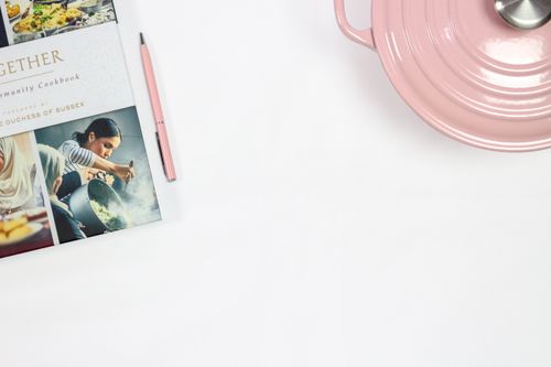 Free A stylish arrangement featuring a cookbook, pen, and pink cooking pot on a white surface. Stock Photo