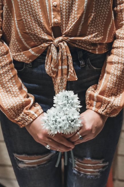 A stylish woman in ripped jeans and a patterned blouse holds white flowers. Perfect for fashion and lifestyle themes.