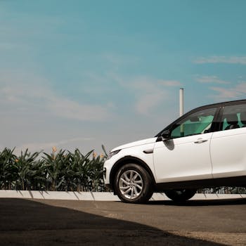 A white SUV parked outdoors with greenery in the background and a clear blue sky.