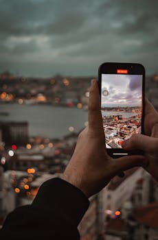 Close-up of hands filming Istanbul skyline with smartphone at dusk.