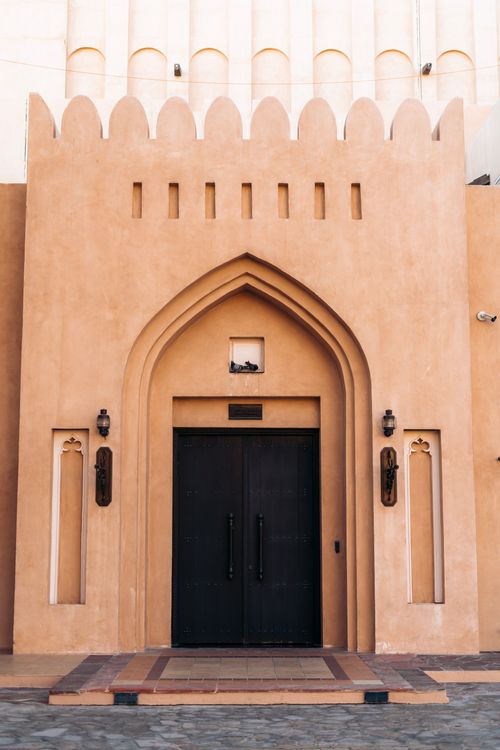 Free Ornate Arabic architectural facade featuring a traditional arched entrance with symmetry and earthy tones. Stock Photo