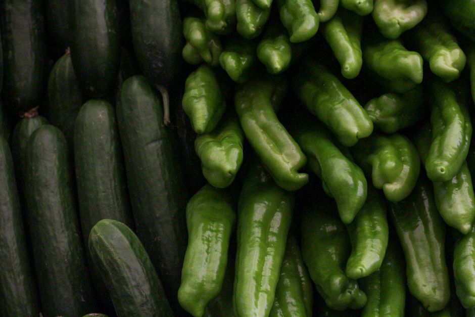 A close-up shot of fresh green cucumbers and Anaheim peppers at a market display, showcasing vibrant green hues.