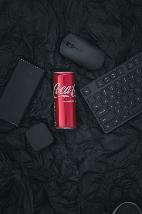 Free Flat lay of Coca-Cola can surrounded by tech gadgets on a textured black background. Stock Photo