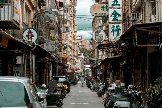 Urban scene featuring cars and motorcycles on a busy street lined with shops in an Asian city.