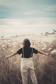 Young woman with open arms enjoying a serene summer day in a grassy field.