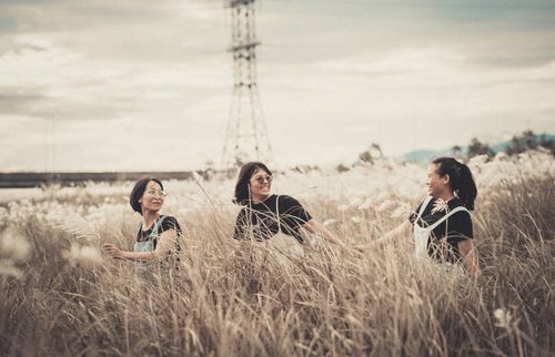 Free Three Asian women enjoying a stroll through a tall grass field on a cloudy day. Stock Photo