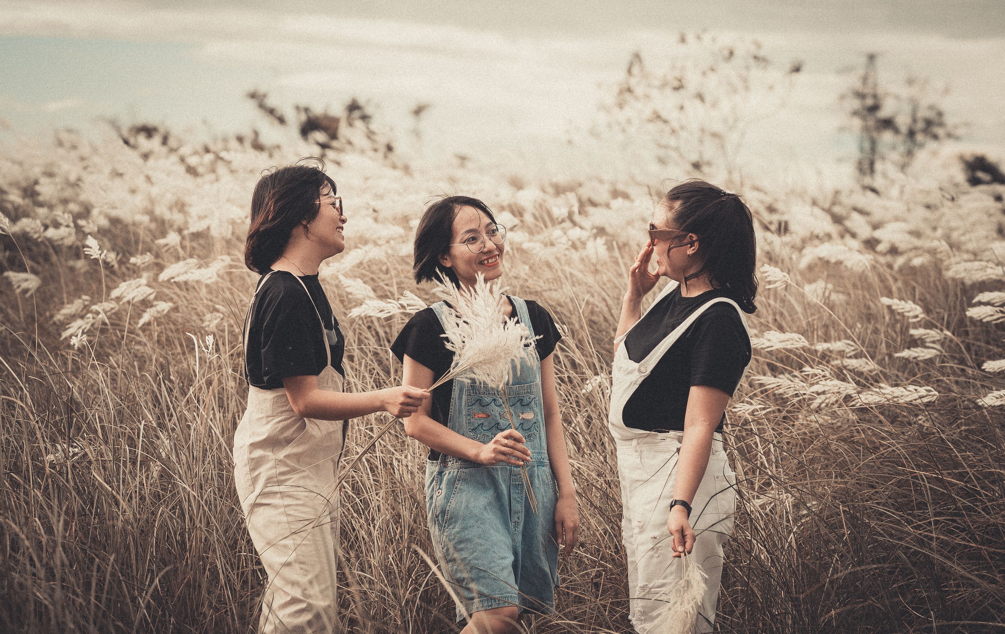 Three women standing and smiling in a peaceful meadow, captured in warm tones.