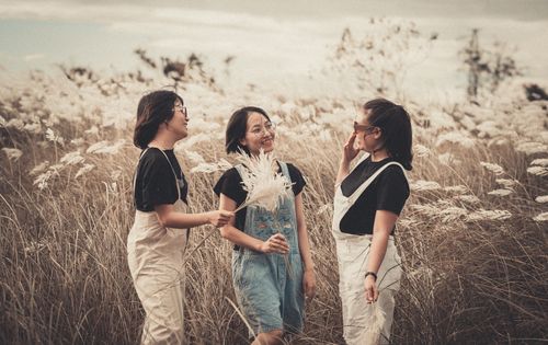 Free Three women standing and smiling in a peaceful meadow, captured in warm tones. Stock Photo