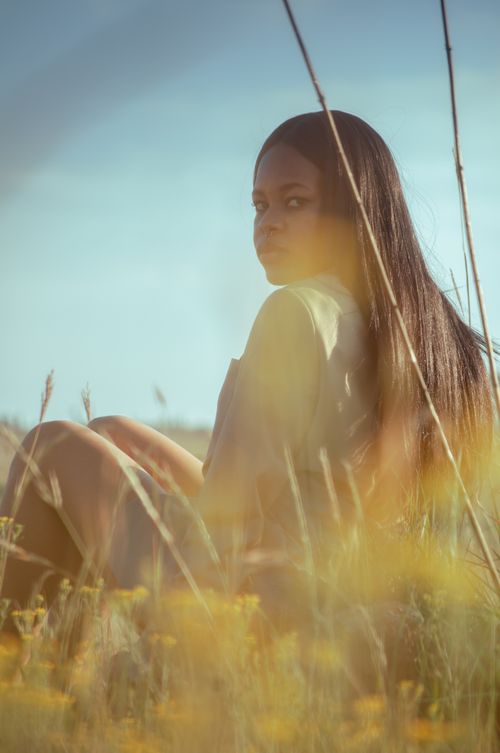 Free A contemplative African American woman sits in a tranquil field, surrounded by nature. Stock Photo