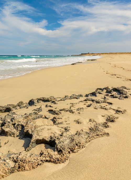 Free Golden sandy beach with rocks and gentle waves under a bright blue sky. Stock Photo