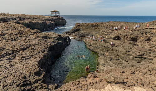 People on a Rocky Shore and Swimming in a Bay