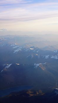 A stunning aerial view of snowcapped mountains shrouded in mist at sunrise, capturing nature's serene beauty.