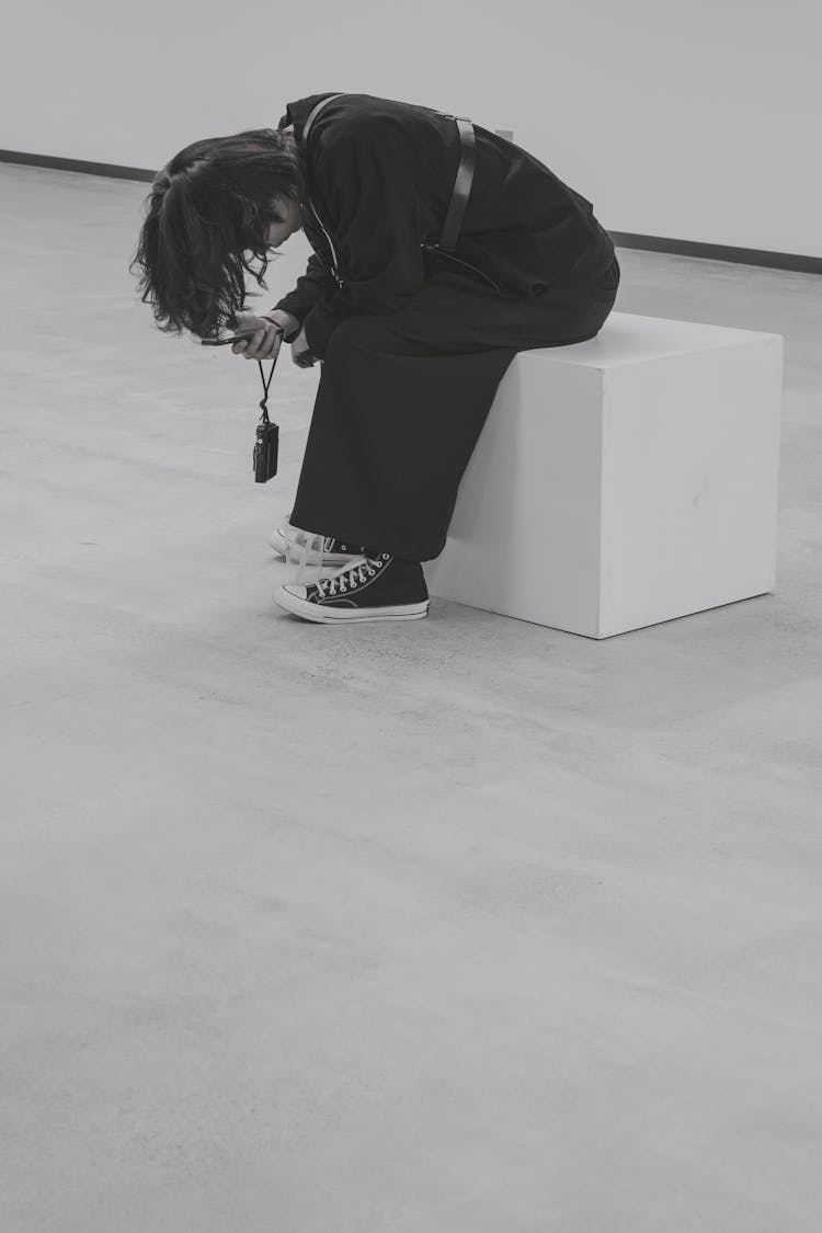 Black And White Photo Of A Person Sitting On A Box Using Smartphone