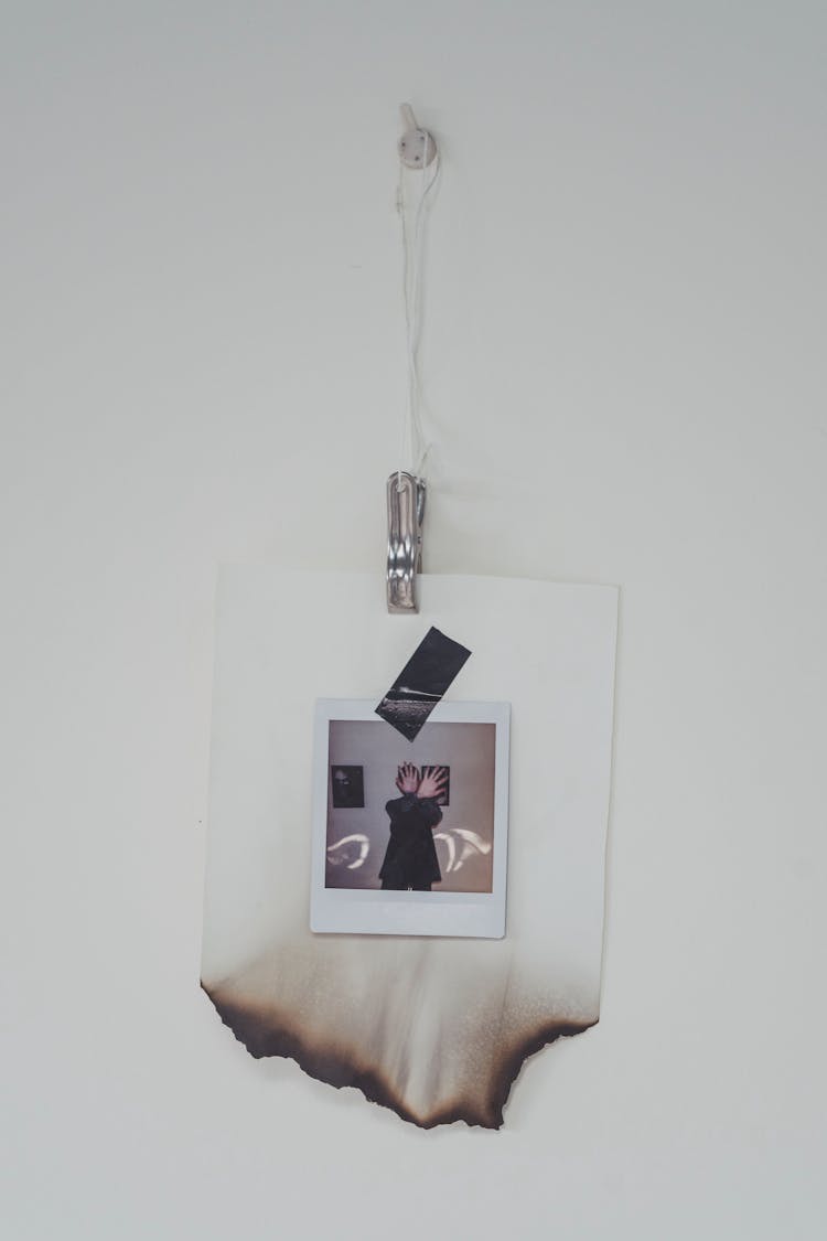 Installation Of A Polaroid Photo With Burned Passepartout Hanging On A White Wall