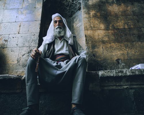 Free An elderly man with a beard sits in a traditional outfit, holding prayer beads. Stock Photo