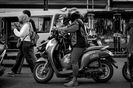 Black and white image of a bustling street with a motorcyclist and pedestrians.
