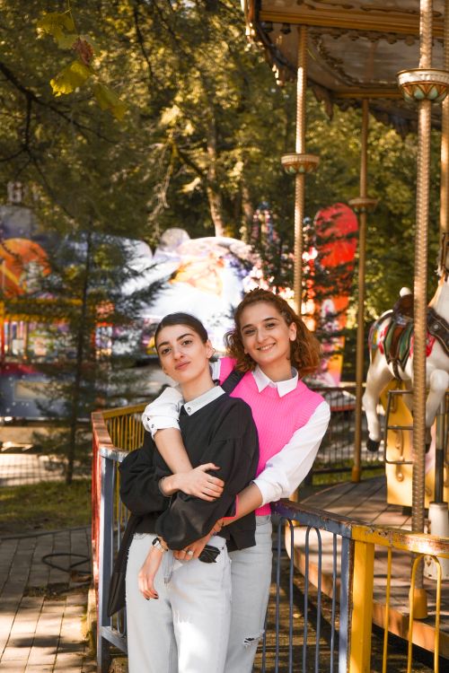Free Two smiling teenagers standing by a carousel in a sunny urban park. Stock Photo