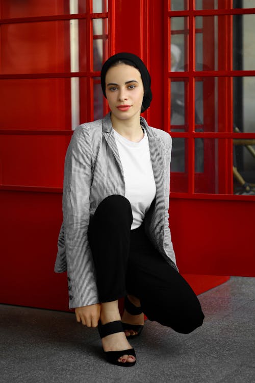 A Young Woman in a Stylish Outfit Crouching near a Telephone Booth