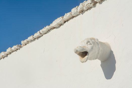 Close-up of a gargoyle's head on a white wall with clear blue sky in Lanzarote, Spain.