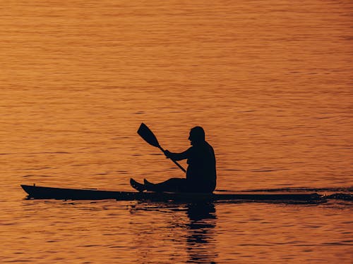 Silhouette of Man Riding a Boat on Body of Water