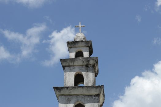 A historic church tower in Dzemul, Mexico with a prominent stone cross under blue skies.