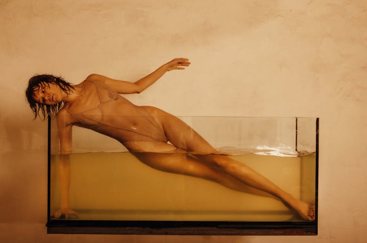 Photo Of A Young Woman Posing In A Glass Tank Filled With Water