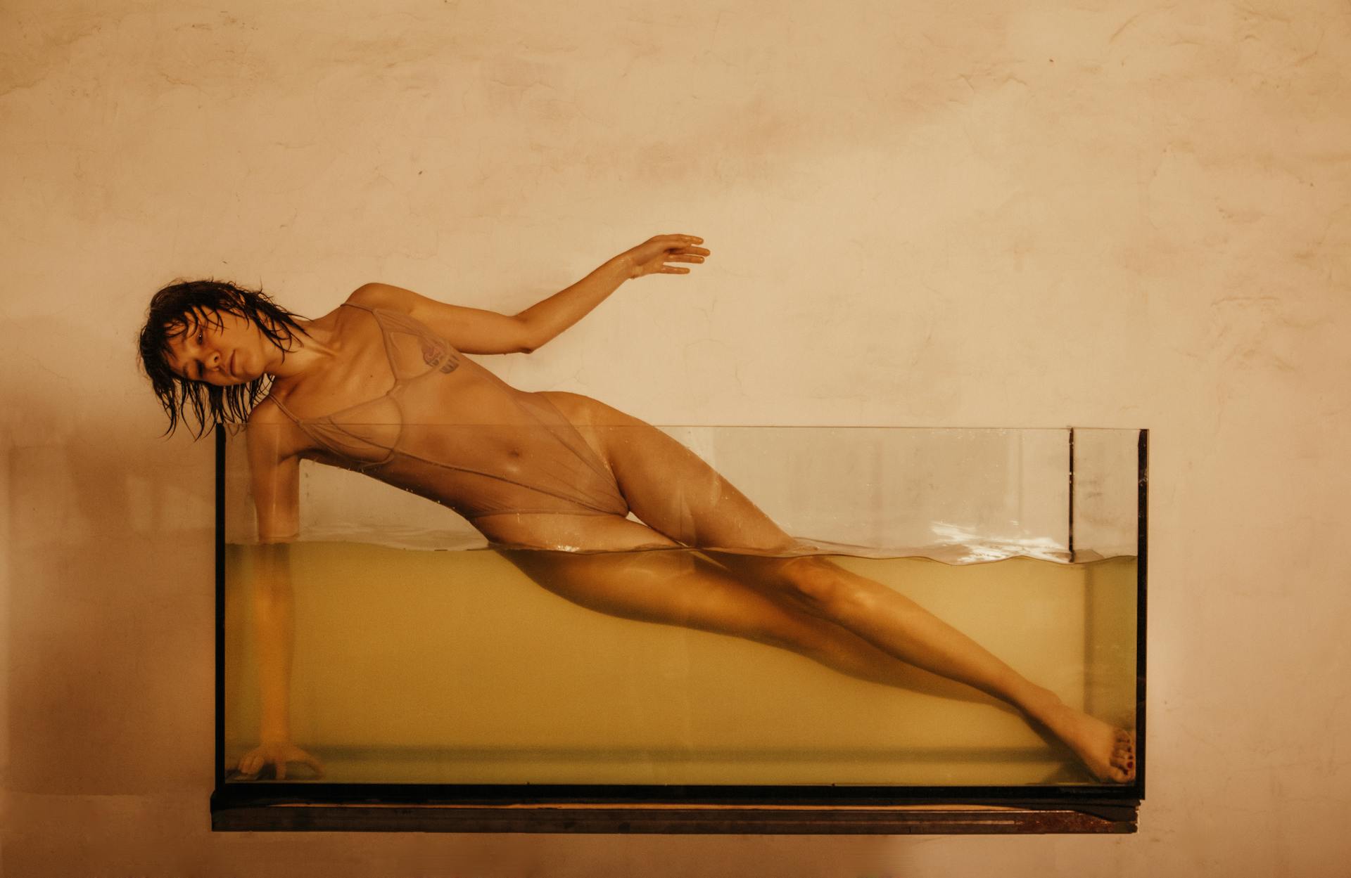 Photo of a Young Woman Posing in a Glass Tank Filled with Water