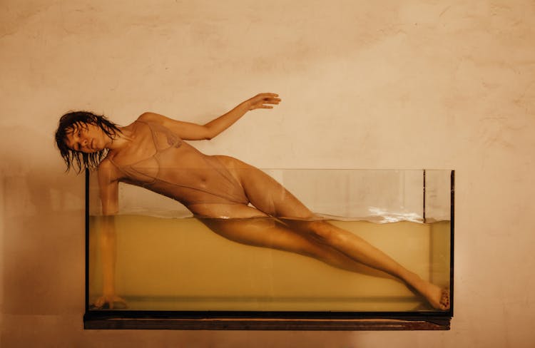 Photo Of A Young Woman Posing In A Glass Tank Filled With Water