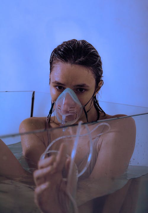 Posed Photo of a Young Woman Sitting in a Glass Tank Filled with Water and Wearing an Oxygen Mask