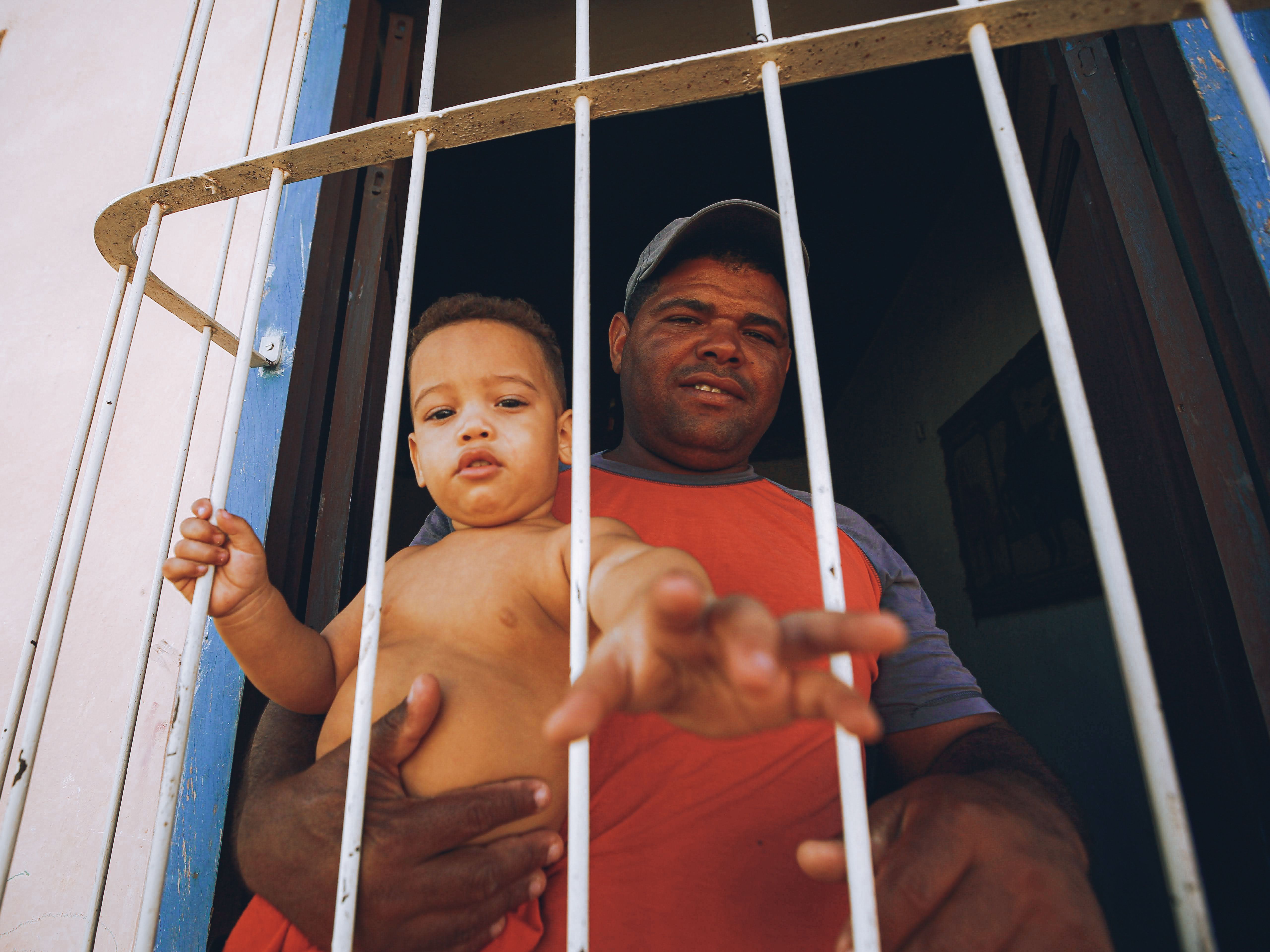 A man holding a baby looks out from behind window bars.