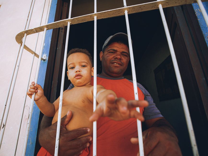 A man holding a baby looks out from behind window bars.
