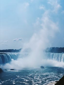 Spectacular view of the majestic Niagara Falls with a sightseeing boat approaching the waterfall.