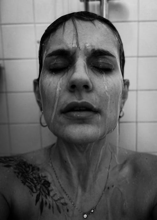 Black and White Photo of a Woman Standing in a Shower with Eyes Closed 