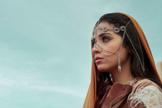 Portrait of a Middle Eastern woman wearing traditional jewel-adorned veil against a clear sky.