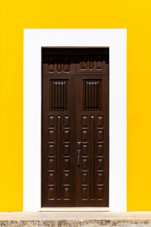 Free A brown wooden door set in a bright yellow wall with a white frame, showcasing vivid contrasts. Stock Photo