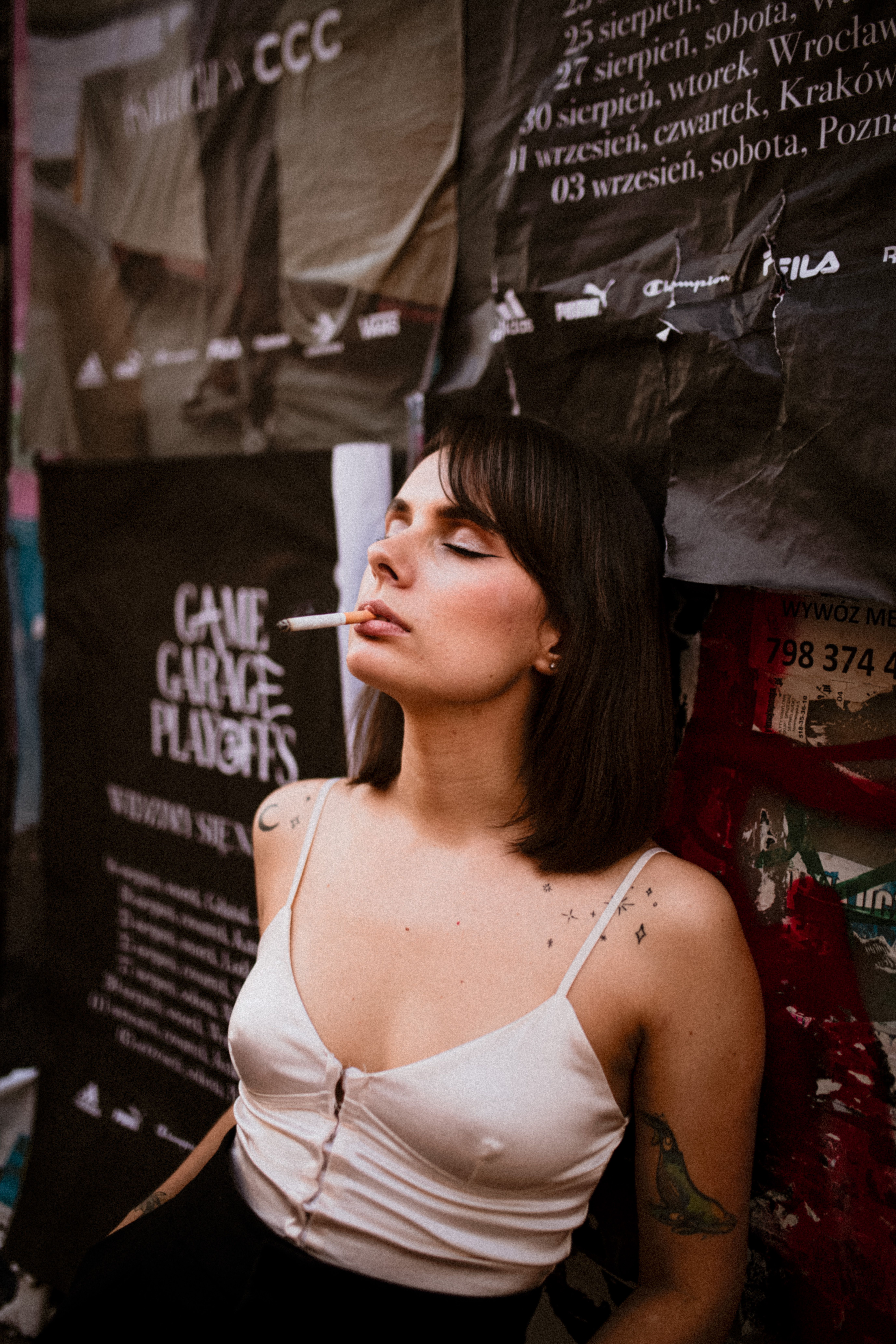 Portrait of a woman smoking a cigarette against urban posters, exuding a rebellious vibe.