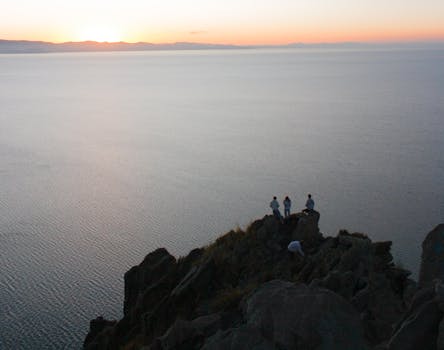A mesmerizing sunset view over Lake Titicaca with people standing on a rocky cliff in Copacabana, Bolivia.