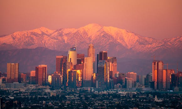 Stunning view of Los Angeles skyline with snow-capped mountains at sunset.
