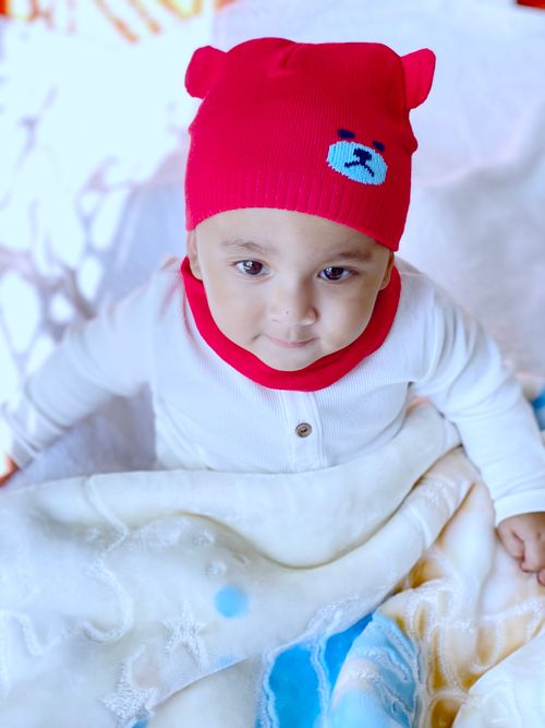Free Cute baby with red beanie and white attire sitting on a patterned blanket. Stock Photo