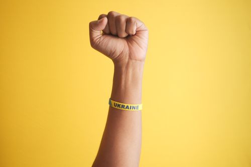 Free Close-up of a fist with a Ukraine wristband against a bold yellow background, symbolizing strength and unity. Stock Photo
