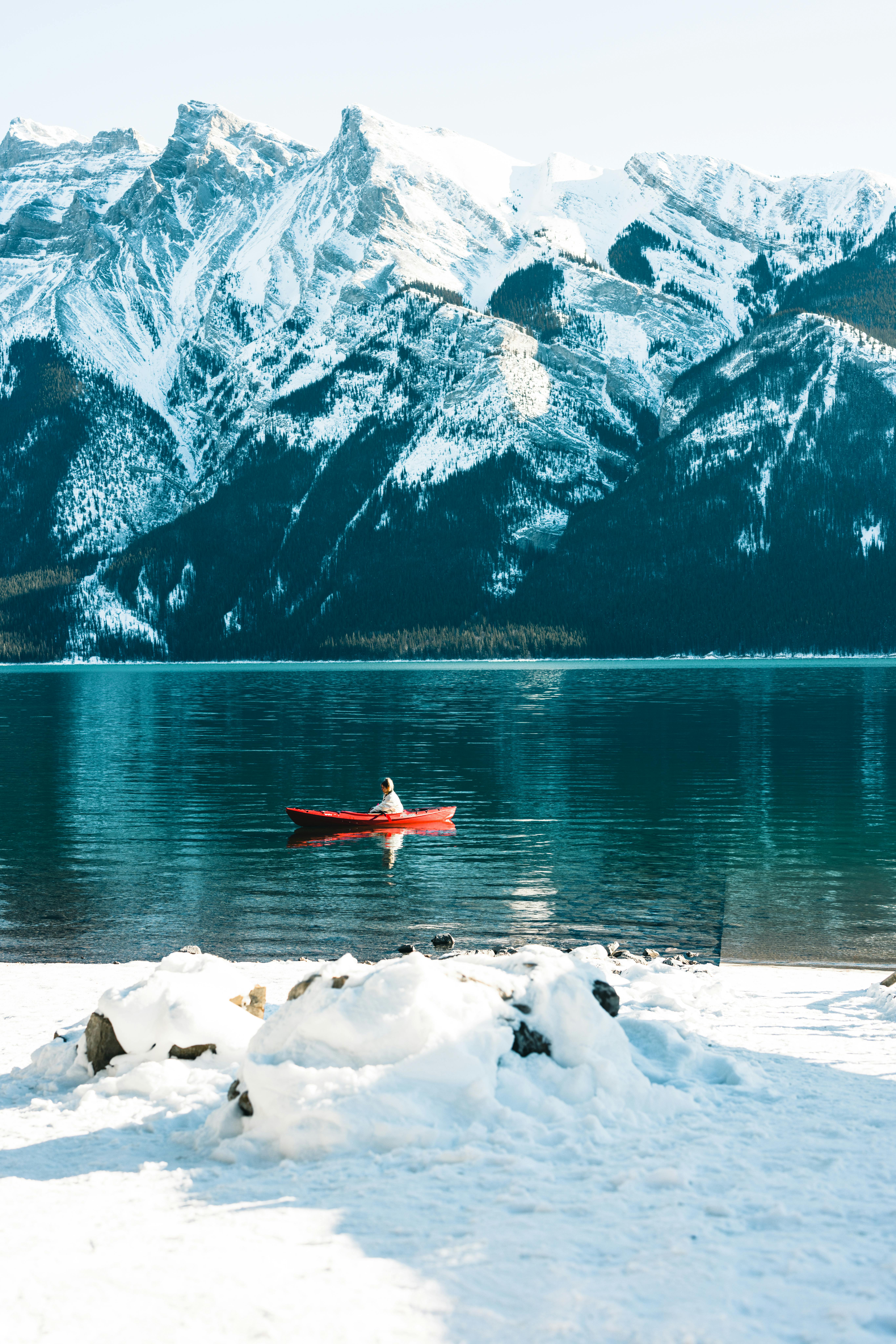 Experience the tranquil beauty of a kayak on Lake Minnewanka amidst snow-covered peaks in Banff, Canada.