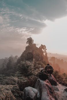 一位独身的徒步旅行者在雾霭笼罩的山峰上，享受着日出时分的宁静，四周是令人叹为观止的自然风光